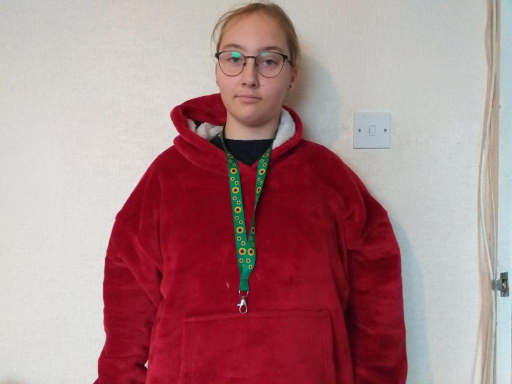 The picture shows a girl. She is wearing a red hoodie. She is also wearing a sunflower lanyard