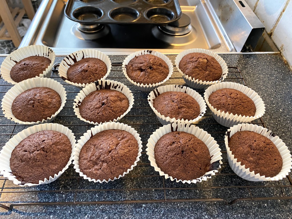 Freshly baked chocolate cupcakes in paper liners cooling on a wire rack.